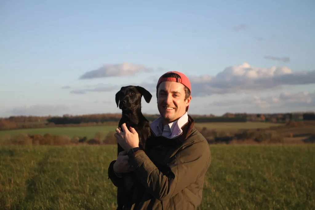 Farmer, stook in field holding black dog in arms