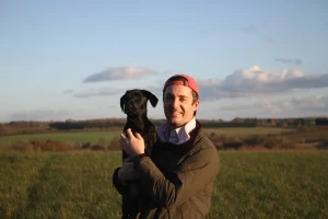 Farmer, stook in field holding black dog in arms